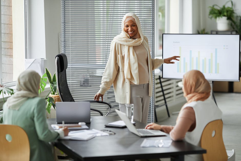 A diverse group of businesswomen in hijabs discussing data in a modern office setting.
